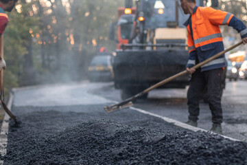 Road construction worker leveling asphalt with a shovel. Focus on foreground