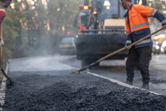 Road construction worker leveling asphalt with a shovel. Focus on foreground