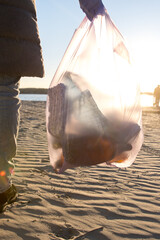 Girl in a winter coat picking up trash on a sandy beach at sunset. The image captures the...