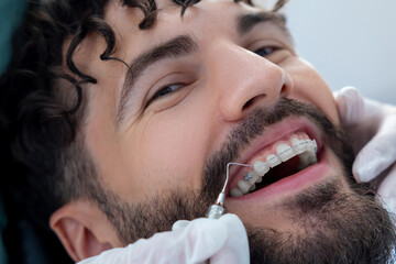 Doctor in dental clinic wearing gloves carefully inspecting patient’s mouth with precise...