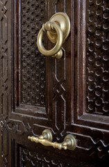 A beautiful ornate door with lattice patterns and a brass handle and door knocker.