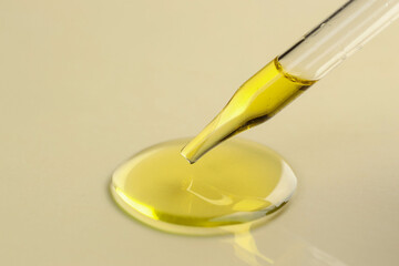 Cosmetic oil dripping from pipette on dark beige background, closeup. Space for text
