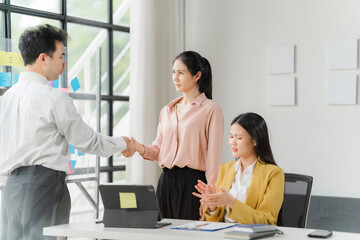 Business Deal Closed:  A confident businessman shakes hands with a female colleague, sealing a deal while another woman looks on in the modern office setting.  