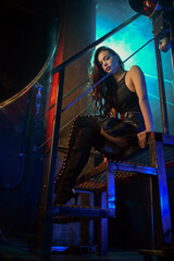 Beautiful girl with dark long hair posing on an old iron factory background. Cyberpunk concept.