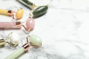 Face rollers on white marble background, closeup. Space for text