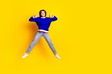 Full length photo of pretty teen girl jumping thumb up wear trendy knitwear blue outfit isolated on yellow color background