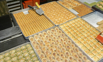 Variety of freshly made Turkish baklava displayed in trays at a shop. Different shapes and flavors of baklava are ready to be served.