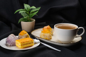 Closeup view coffee in white ceramic cup with chinese pastry moon cake in white ceramic dark edge tray, colorful chinese pastry moon cake and layer cake in white ceramic dish on black background.