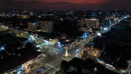 Crowds gather around a lively city square filled with lights and activity after sunset