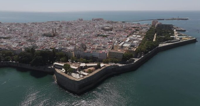 Aerial drone wide cityscape of C&aacute;diz in Spain, Andalusia, Europe, on bright sunny day, facing San Sebastian castle fortress and lighthouse and Baluarte de la Candelaria. Shot in 5K ProRes 422 HQ