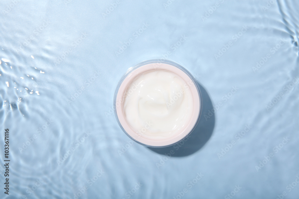 Poster Cosmetic product. Jar with cream in water on light blue background, top view