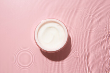 Cosmetic product. Jar with cream in water on pink background, top view