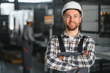 Men industrial engineer wearing a white helmet while standing in a heavy industrial factory behind