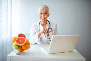 Senior Doctor Smiling at Desk with Laptop and Fresh Fruits