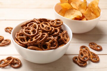 Delicious pretzel crackers and chips on white wooden table, closeup