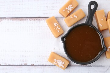 Tasty salted caramel in gravy boat and candies on white wooden table, top view. Space for text