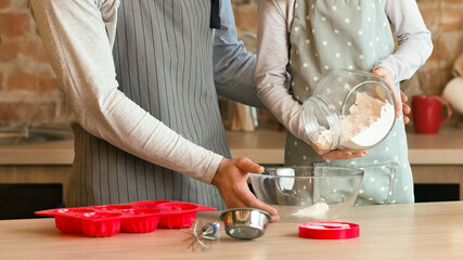 Little girl helping her father to bake, adding flour to bowl, preparing dough together in kitchen, free space