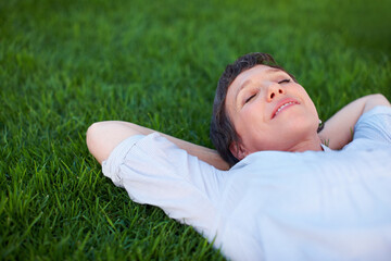 Woman, peace and relax on grass space for comfort, zen and positive mental health. Resting, mature person and smile in nature park for summer travel, freedom and stressless environment for wellness