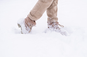 A close-up shot of a person kicking snow dressed in warm winter clothing.