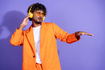 Photo of attractive funny guy wear orange suit listen music earphones dancing emtpy space isolated violet color background