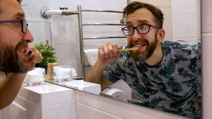 A man brushing his teeth with a wooden toothbrush in front of a bathroom mirror