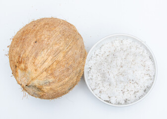 Whole mature coconut fruit with its flakes in ceramic bowl on white background