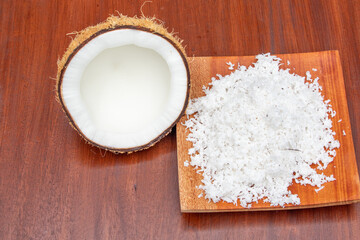 Organic coconut flakes set on wooden board with half cut of mature coconut