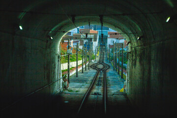 the view from inside a tunnel, looking out onto a narrow-gauge railway track that winds its way...