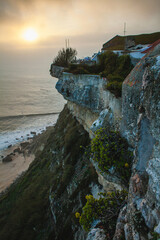 a dramatic seaside cliff, with the sun setting over the horizon, casting a warm golden glow across the ocean.