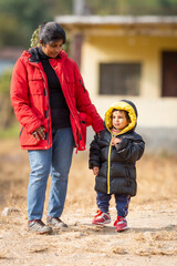Mother baby in warm clothes standing outdoors in holidays morning sunlight