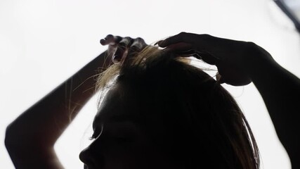 Dancer in silhouette runs her hands through her hair while posing against a bright background, creating a striking visual of elegance and movement in a backlit studio setting