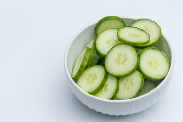 Slices of cucumber in ceramic bowl on white background