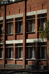 Naklejka premium Color vertical photo, facade of two-story red brick building with metal bars on windows, wooden frames, city background.