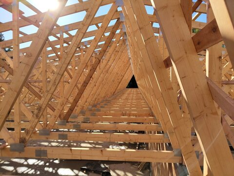 Sunlit view through rows of wooden trusses in a construction site, highlighting the symmetry and strength of the framework
