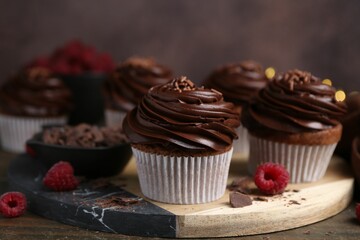Tasty cupcakes with chocolate cream and raspberries on wooden table, closeup