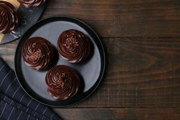 Tasty cupcakes with chocolate cream on wooden table, top view. Space for text