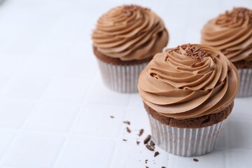 Tasty cupcakes with chocolate cream on white tiled table, closeup. Space for text