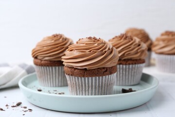 Tasty cupcakes with chocolate cream on white tiled table