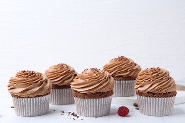 Tasty cupcakes with chocolate cream on white tiled table, space for text