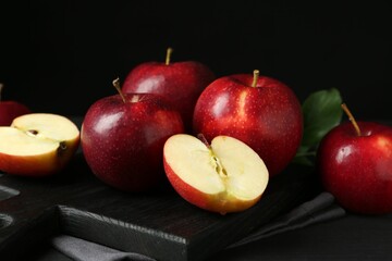 Whole and cut fresh ripe red apples on black wooden table, closeup