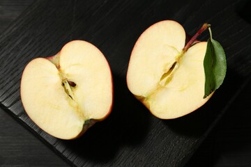 Halves of fresh ripe apple with green leaf on black wooden table