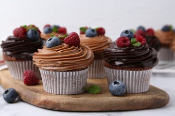 Tasty cupcakes with chocolate cream and berries on white marble table, closeup