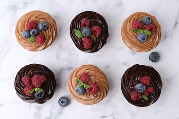 Tasty cupcakes with chocolate cream and berries on white marble table, flat lay