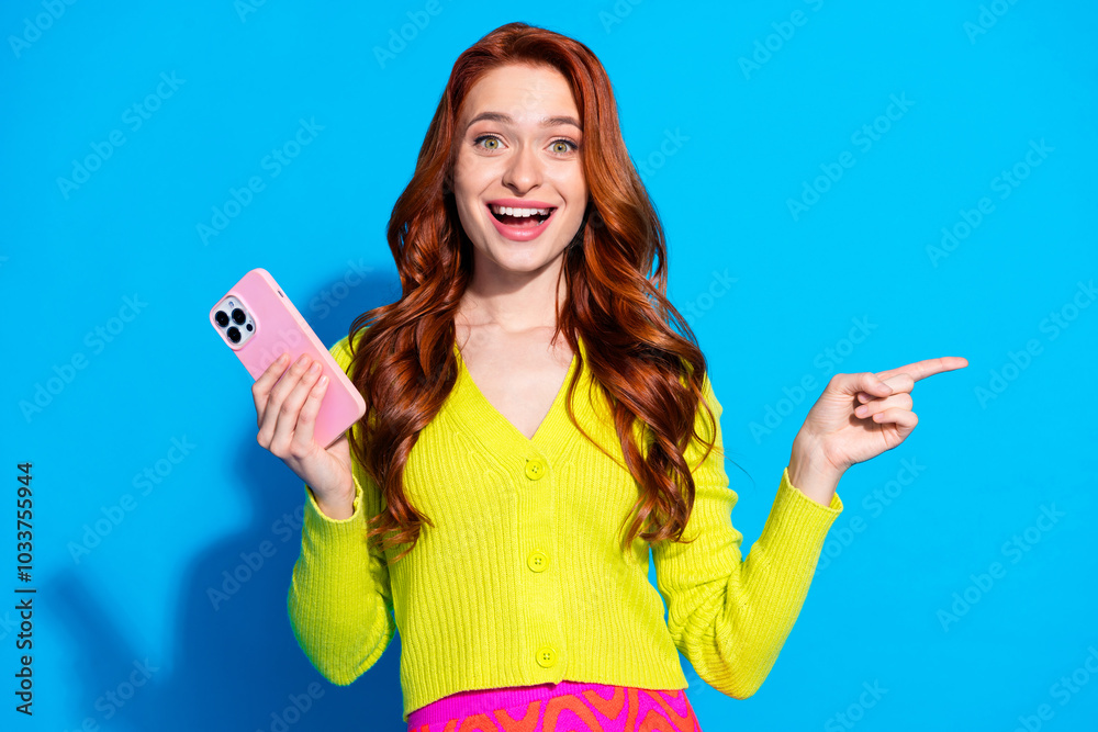 Wall mural Photo portrait of pretty young girl hold gadget excited point empty space wear trendy yellow outfit isolated on blue color background