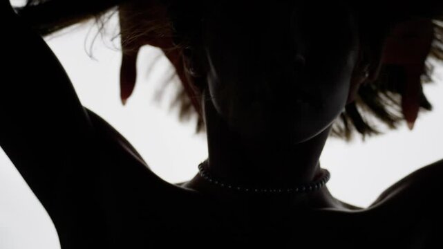 Silhouette of a young woman adorned with a pearl necklace, gracefully dancing and flowing her hair, exuding elegance against a stark white backdrop