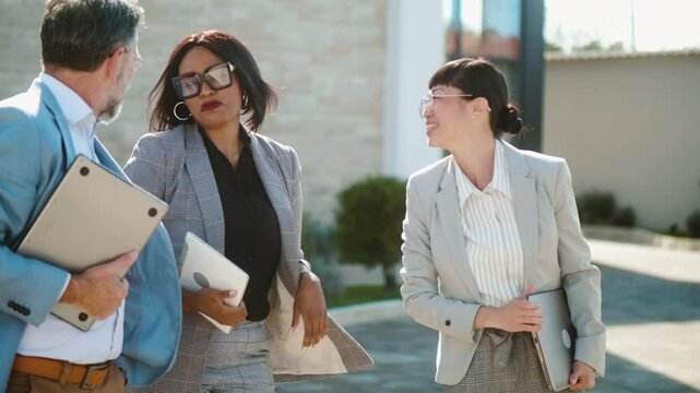 Smiling black businesswoman talking with multiracial colleagues after work leaving the building. Asian businesswoman smiling talking to a group of multiracial colleagues while walking outdoors