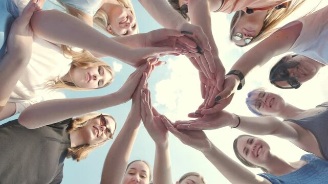 Young schoolchildren join hands in a circle against the backdrop of a summer sky.