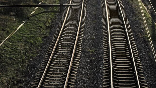 From above, one can see a series of parallel train tracks flanked by lush greenery beneath a bright sunny sky