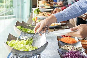 Hands of a young Asian women are selecting salad ingredients at buffet restaurant.