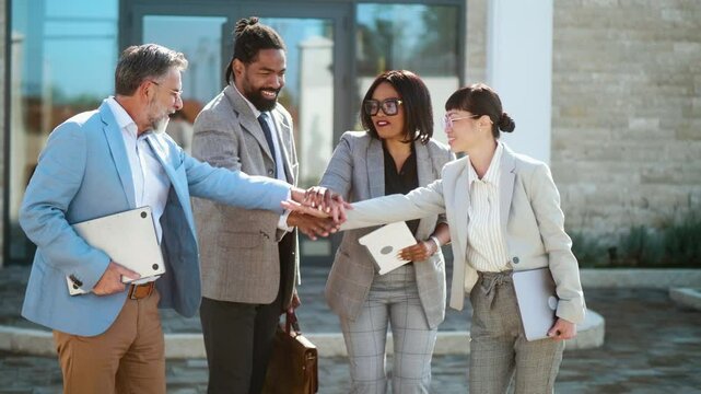 Successful multiracial business team people stack hands in pile in front of building, raise hands and celebrate success and victory in business outdoor together